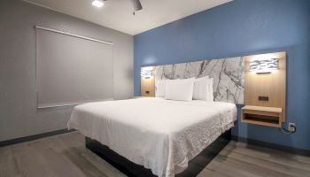 A modern bedroom with a large bed, white linens, blue and gray walls, and built-in bedside lights on a marble-look headboard.