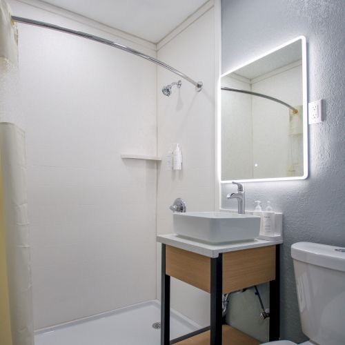 A modern bathroom with a shower, vanity with sink, illuminated mirror, and toilet on a gray tiled floor.