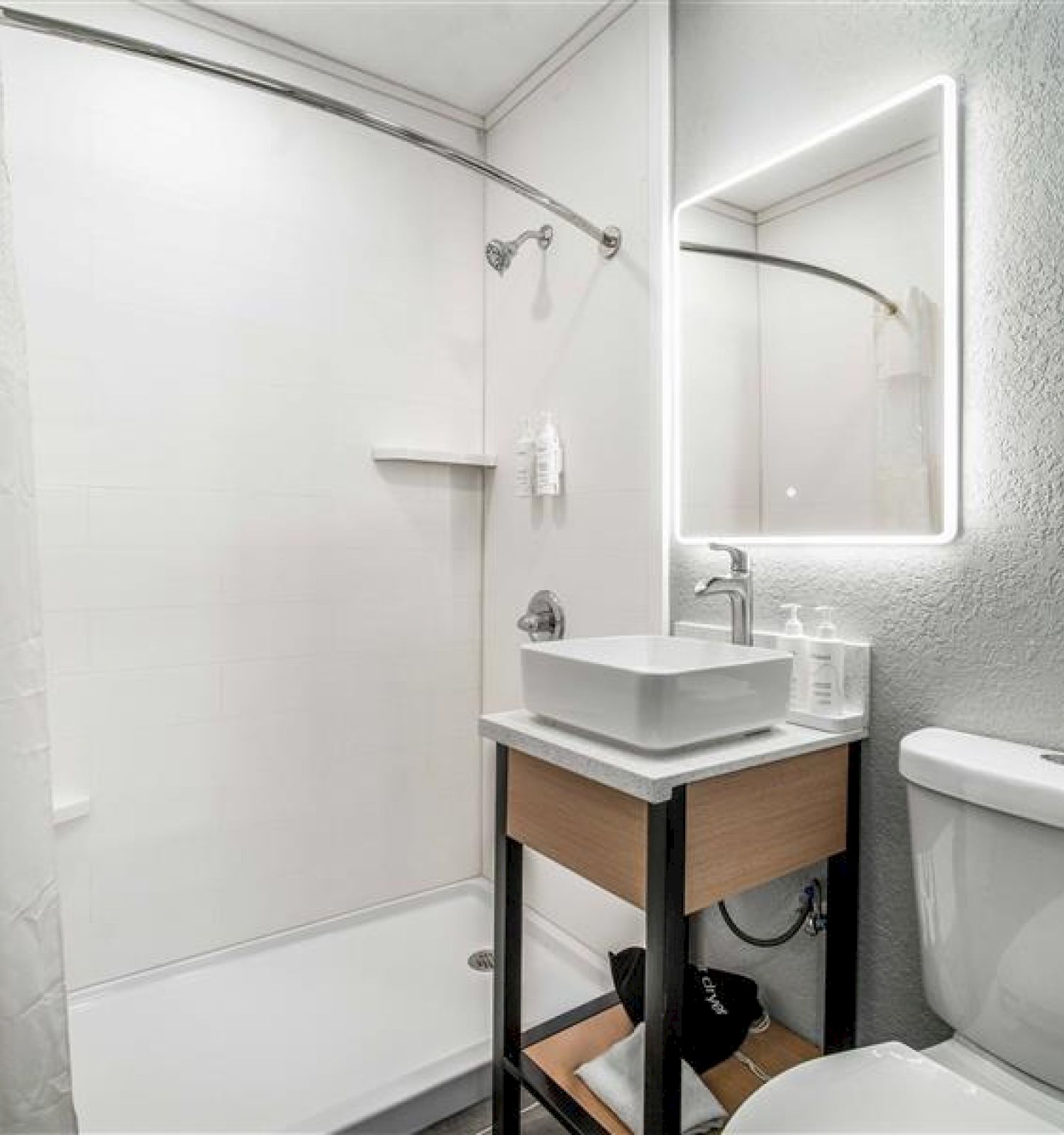 A modern bathroom with a shower, lit mirror, sink, and toilet. Towels hang on the wall. The space is clean and minimalistic.