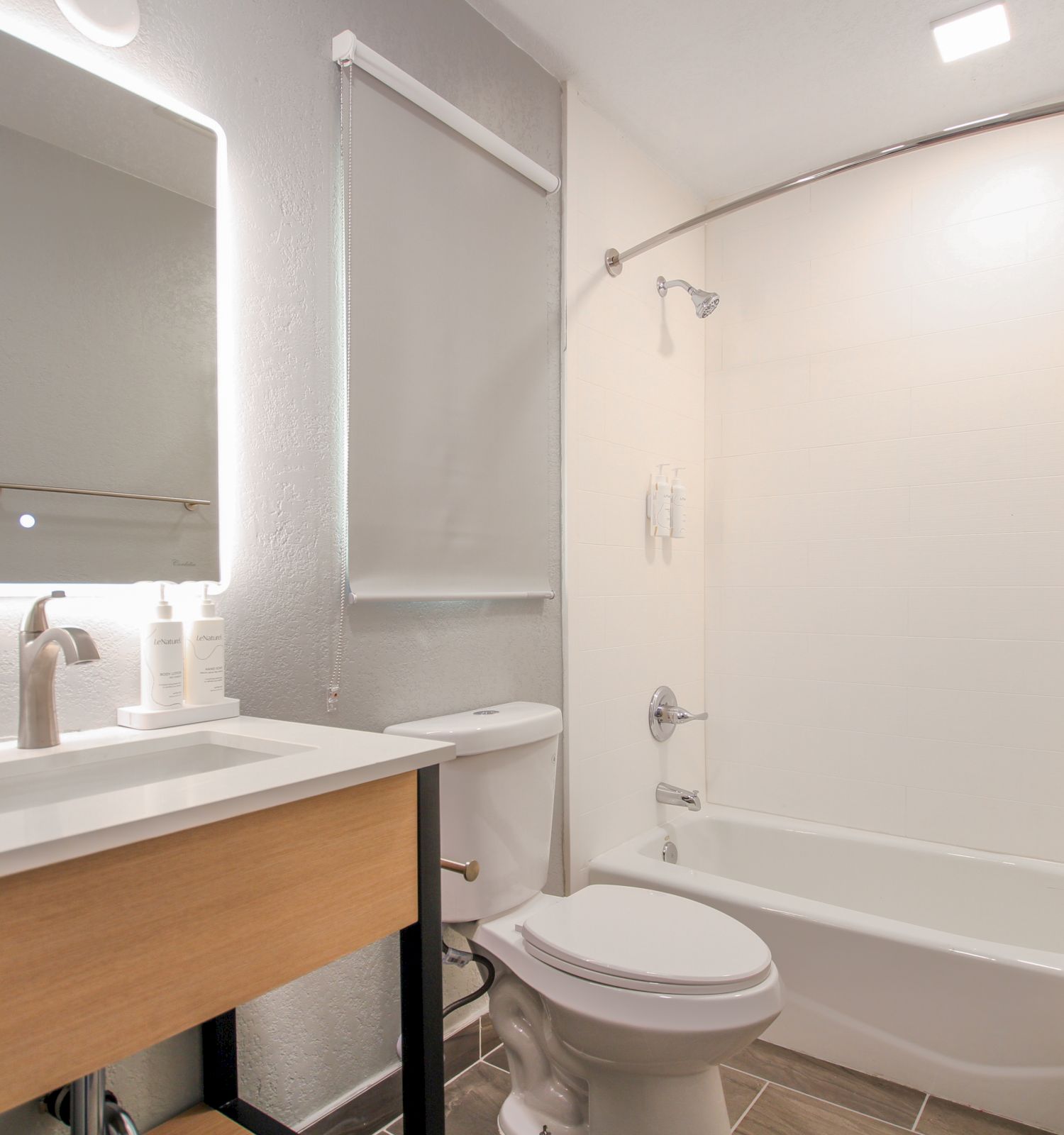 This image shows a modern bathroom with a sink, mirror, toilet, and bathtub with a shower curtain. The space is clean and well-lit.