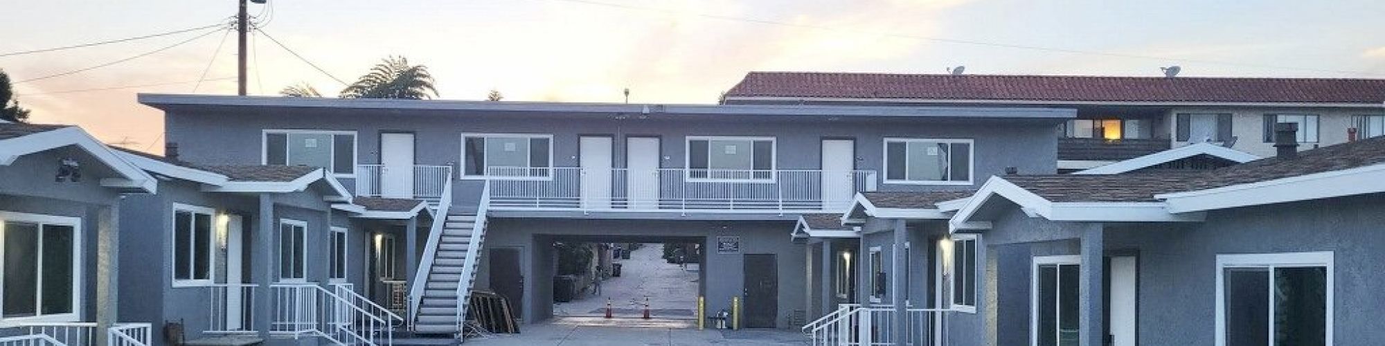 The image shows a small motel or apartment complex with two levels, outdoor stairs, and a central driveway leading to parking spaces.