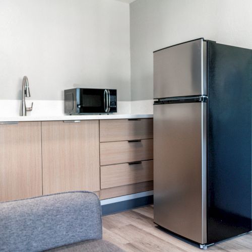 A modern kitchen with light wood cabinets, a microwave, a stainless steel fridge, and a visible sink area.