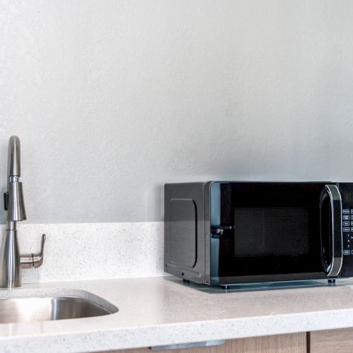 A kitchen counter with a stainless steel sink and faucet on the left, and a black microwave on the right side.