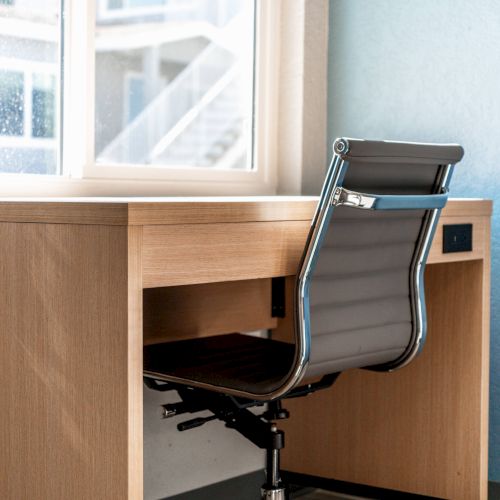 A modern office chair is positioned at a wooden desk next to a window, set against a light blue wall.