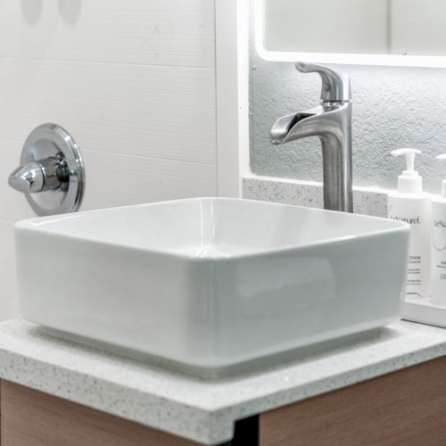 A modern bathroom sink with a chrome faucet, two soap dispensers on the counter, and a wall-mounted fixture in the background.