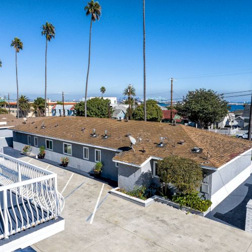 A coastal residential area with single-story buildings, palm trees, and views of the ocean under a clear blue sky.