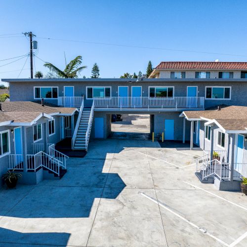 The image shows a small motel with multiple rooms, stairs, and a central courtyard. The building has a blue and gray color scheme.