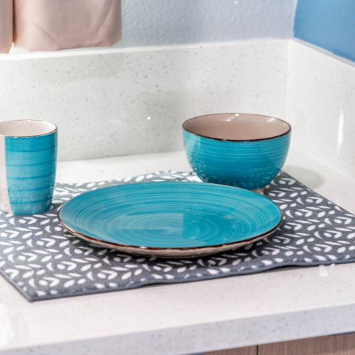 A turquoise mug, plate, and bowl on a patterned mat on a white countertop in a kitchen setting.