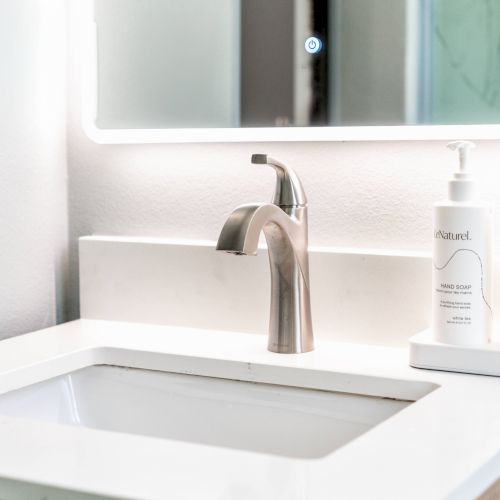 A modern bathroom sink with a sleek faucet and two soap dispensers on the right under a well-lit mirror.