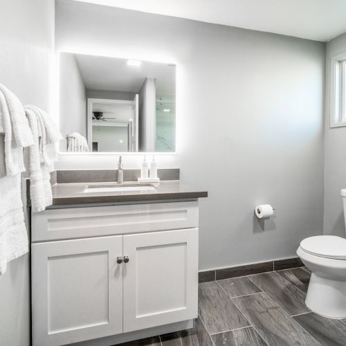 A modern bathroom with a sink, mirror, toilet, towel rack, and window. Neutral tones and sleek design create a clean look.