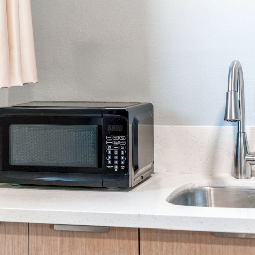 A microwave sits on a kitchen counter next to a sink with a modern faucet and neutral-colored cabinets below.