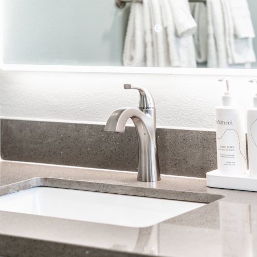 A modern bathroom sink with a sleek faucet, two soap dispensers, and a neatly folded towel in the background.