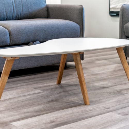 A modern living room features a white, uniquely-shaped coffee table with wooden legs, placed stylishly on a light wood floor between two sofas.