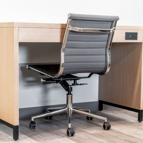 A modern office setup with a wooden desk and a gray ergonomic swivel chair on casters in a minimalist room.