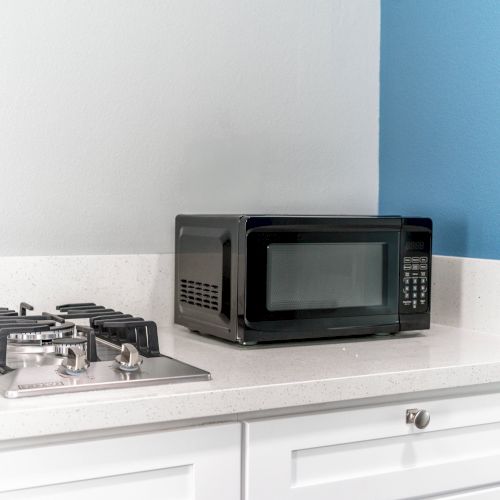 A kitchen counter with a black microwave and a gas stove on a white surface, adjacent to a blue wall.