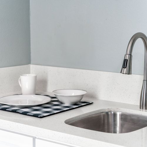 A kitchen counter with a silver faucet, sink, and drying mat holding a plate, bowl, and mug.