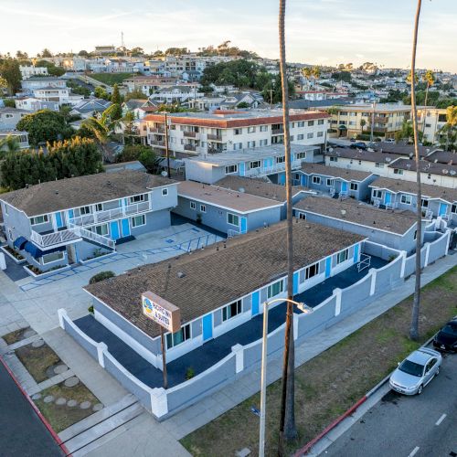 Aerial view of a residential area with multiple buildings, palm trees, and parked cars lining the street.