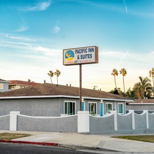 The image shows a motel named Pacific Inn & Suites with a sign and palm trees in the background.