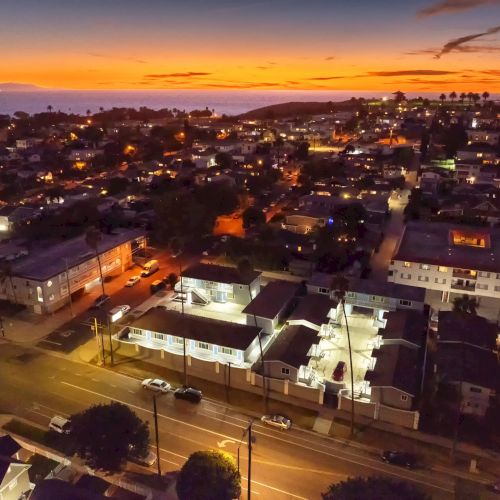 Aerial view of a coastal town at sunset with illuminated streets and houses, overlooking the sea.